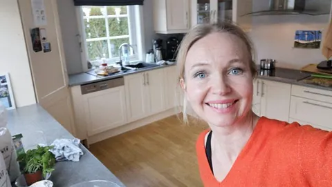 Smilende kvinne med orange genser på kjøkken